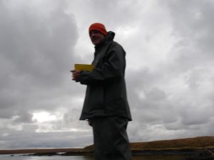 A stormy-grey background with a blurry silhouette of a man in an orange beanie, field notebook, and parka