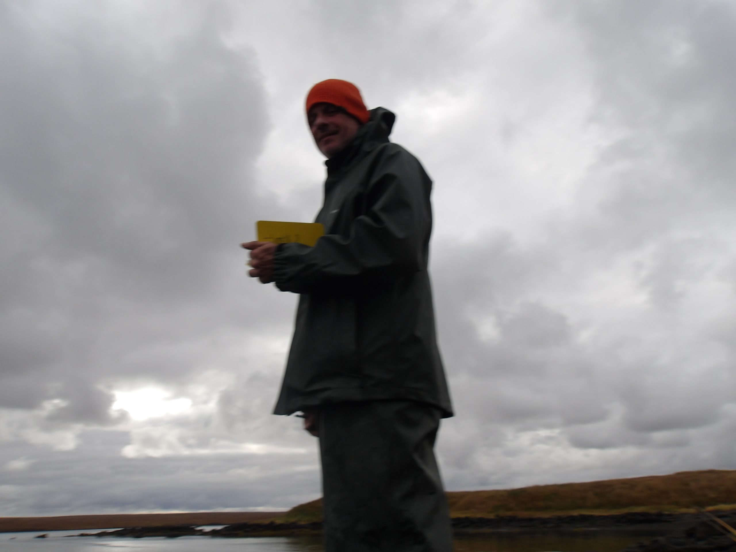 A stormy-grey background with a blurry silhouette of a man in an orange beanie, field notebook, and parka