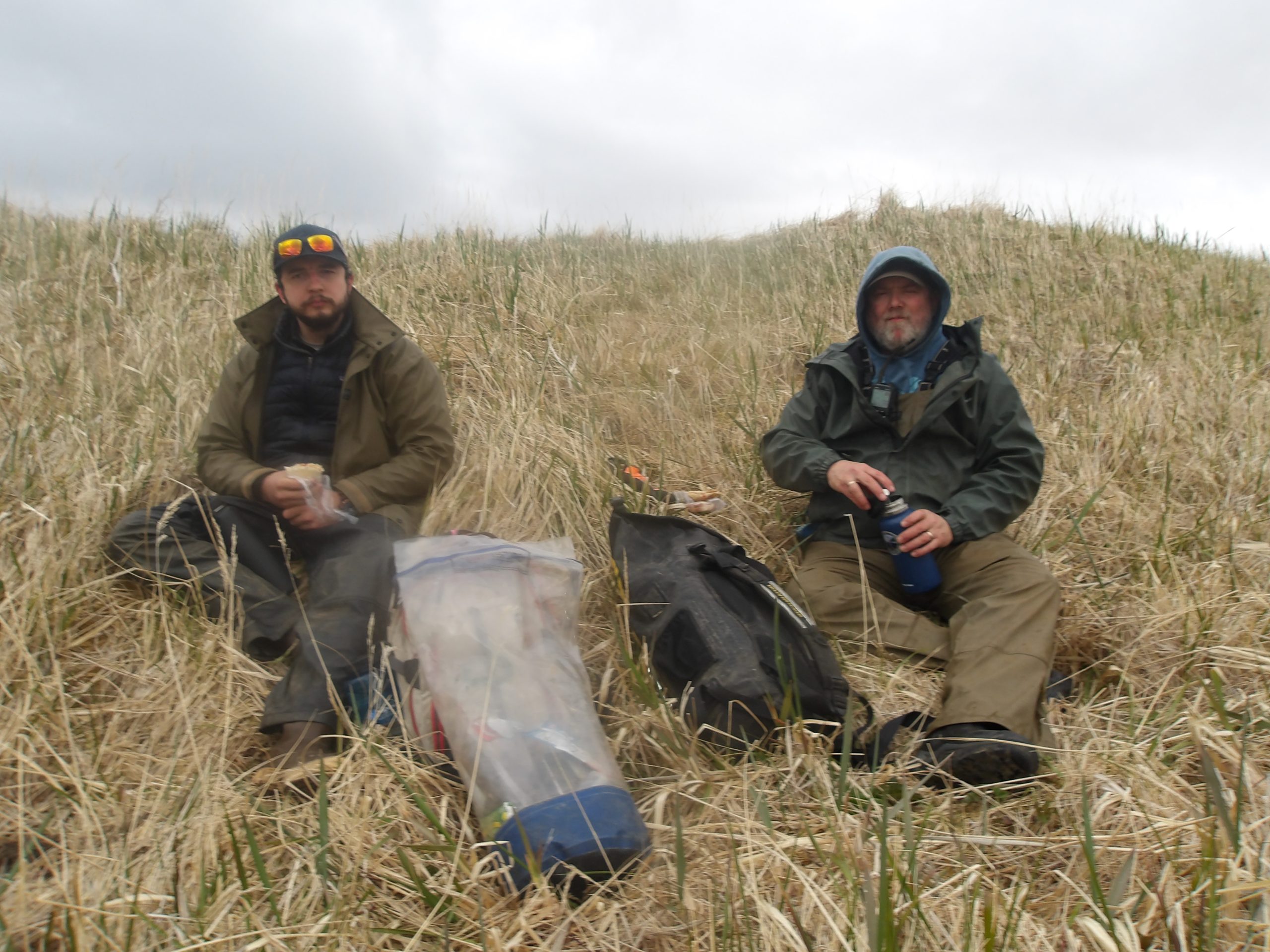 Reyce and Chris sit on small grassy hill, enjoying a lunch break