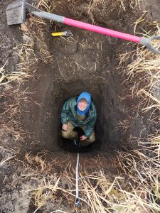 Chris sits at the bottom of a hole looking up at the camera