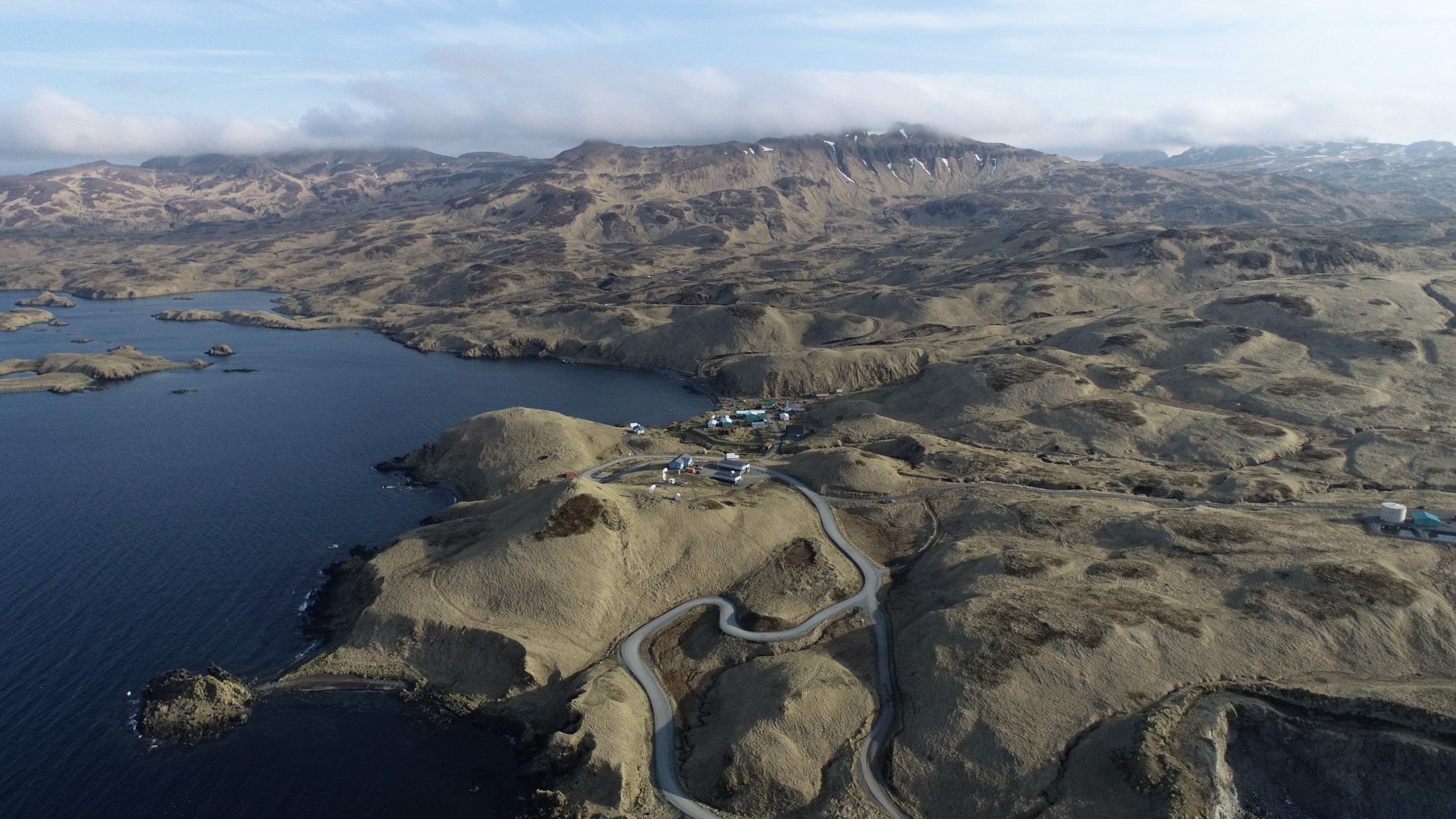 Bird's eye view of Atka centered between golden rolling hills and dark, smooth waters