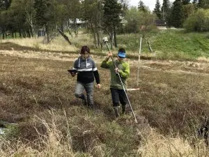 Two people walking through some low brush. One is holding the Trimble stick while the other is holding the Trimble controller. 