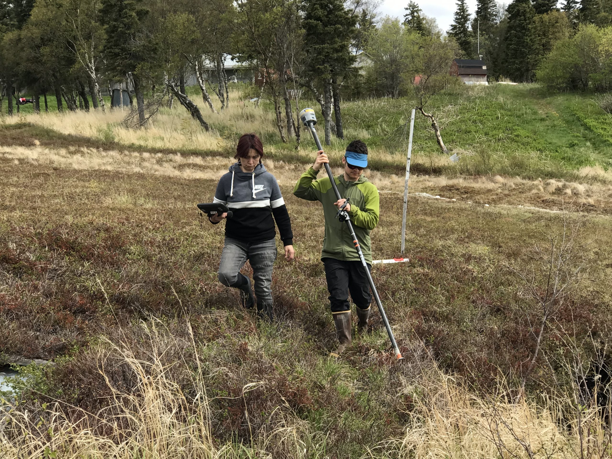 Two people walking through some low brush. One is holding the Trimble stick while the other is holding the Trimble controller. 