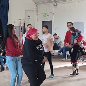 A few people walking in sync and motioning their arms. They are inside a gymnasium. 