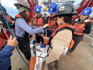 A group of people stand around a large ocean monitoring device. They are standing on a deck.