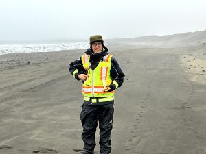 Chris Tran is standing on a sandy beach holding a field notebook. The sky is misty and overcast. 