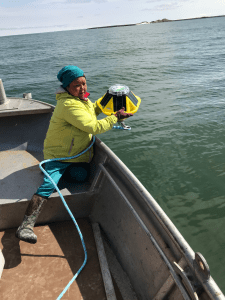 Someone sits in a small metal boat, holding a buoy off to the side, about to put it in the water.