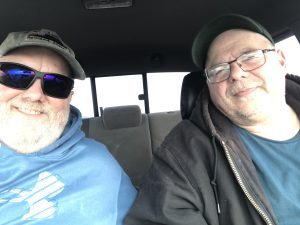 Chris Maio sits in a car next to someone. The windows are whited out.